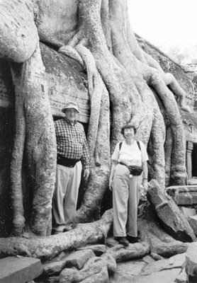 Wayne and Darlene Schild beside giant banyan tree roots at the ruins at Ta Prohm, Cambodia.