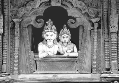A wooden Hindu couple peers from a window high in a temple in Durbar Square.