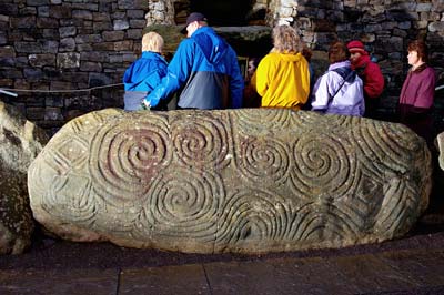 The most elaborately carved kerb stone once covered the entrance to Newgrange.  It now sits in front, part of the band of huge slabs around the tomb. — Photo courtesy of Ken Williams