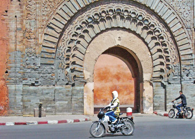 A Moroccan woman on a motorbike rides past the massive gateway of Bab Agnaou in Marrakesh.