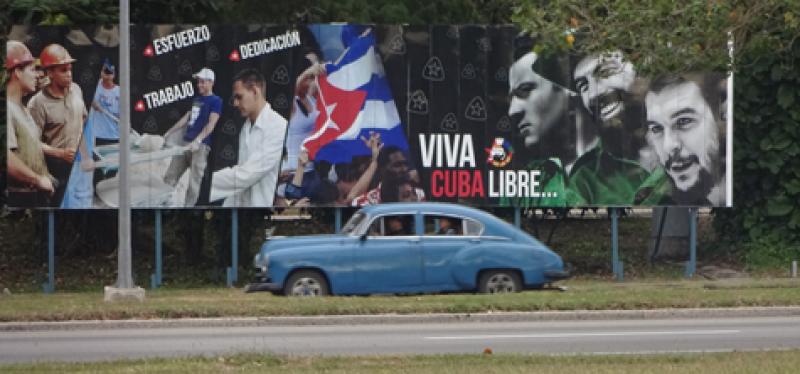 One of the many classic cars that can be found in Cuba, here driving past a political billboard, another common sight.