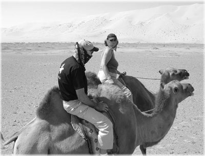 Margo and Herschell Lewis on camelback in the Gobi Desert. Kercheifs keep the blowing sand out of their faces.