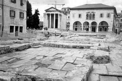 Roman Forum under excavation, with Temple of Augustus and 13th-century town hall in the background.