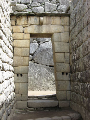 Viewed from inside, this trapezoidal doorway shows a stone ring at the top and bar holds at the sides — Machu Picchu.