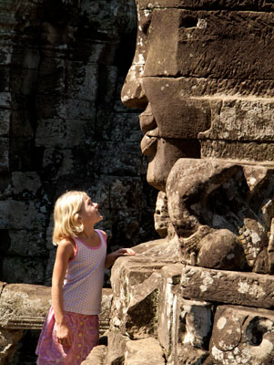 A young girl smiles back at one of the giant carved stone heads at Bayon in Angkor Thom, Cambodia.