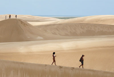 Swirls of white sand flow across the dunes, dwarfing hikers in Lençóis Maranhenses National Park. Photo: Maurice Black