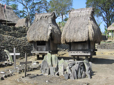 Two bhaga huts representing female spirits. Notice the combination of ancestral stones and Christian crosses at this village cemetery.