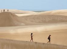 Swirls of white sand flow across the dunes, dwarfing hikers in Lençóis Maranhens