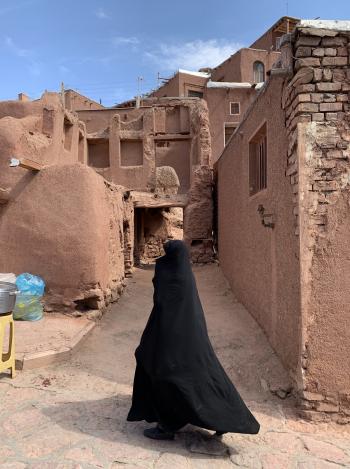 A woman walking through the red-soil village of Abyaneh.